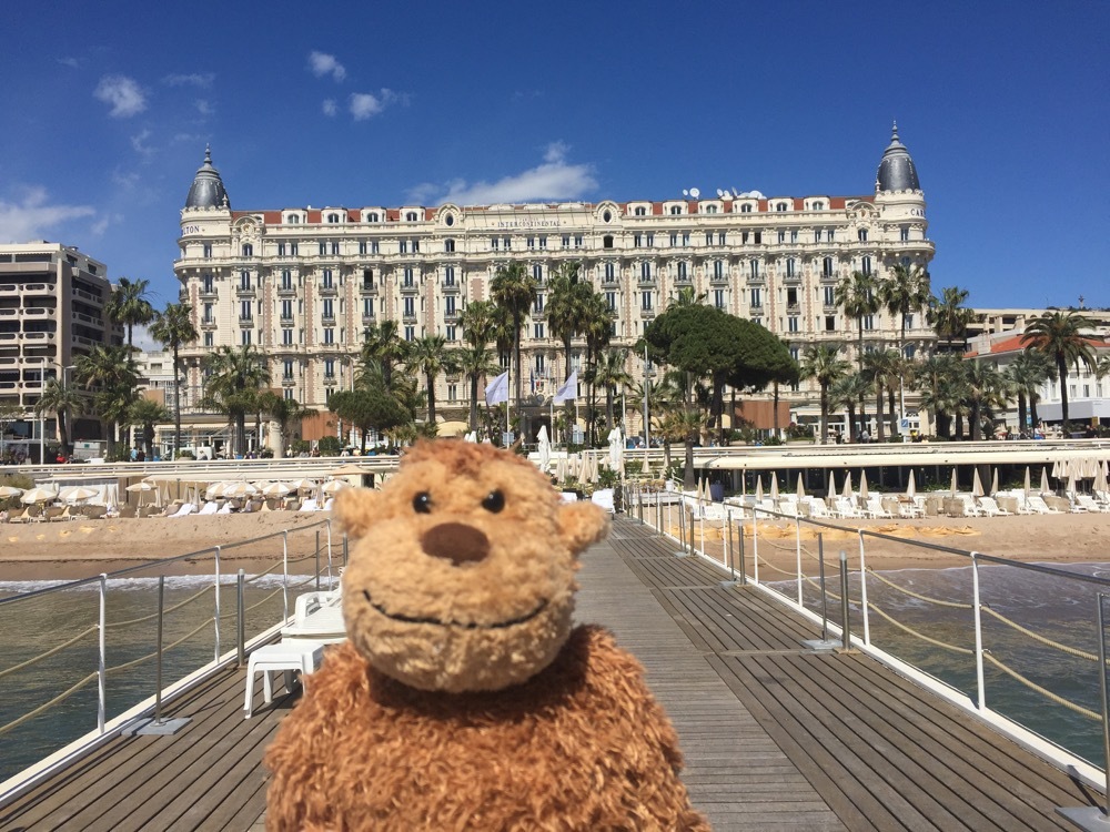 a stuffed animal on a dock with a large building in the background
