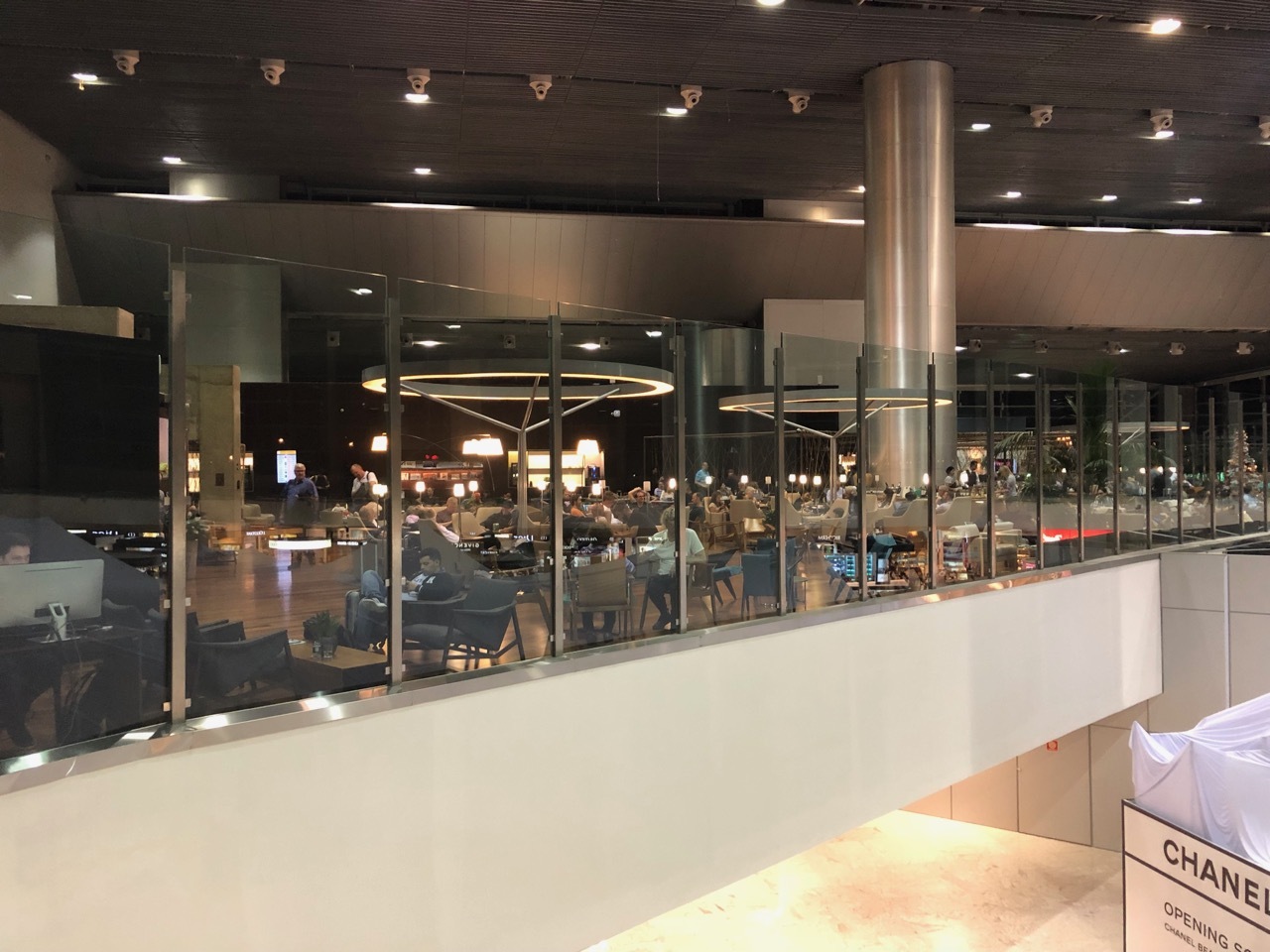 a glass wall with a large ceiling and a large building with people sitting at tables