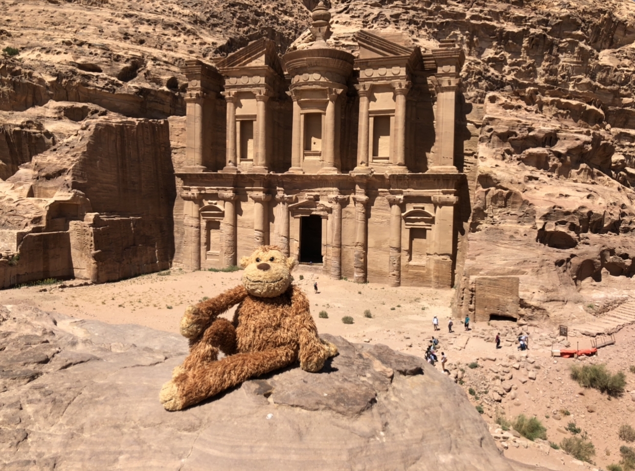 a stuffed animal sitting on a rock in front of a stone building with Petra in the background
