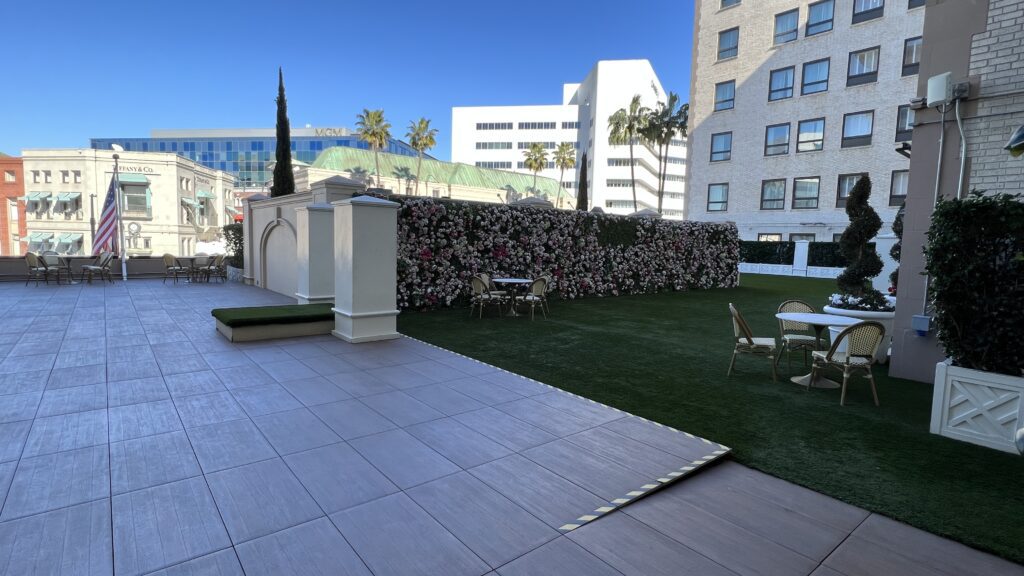 a patio with a wall and chairs in the middle of a green lawn