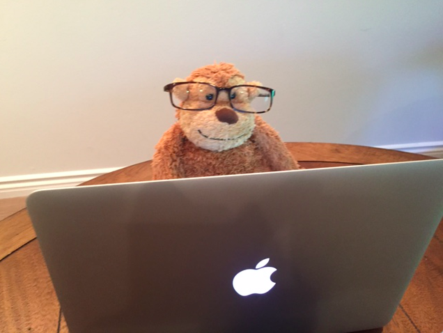 a stuffed animal wearing glasses sitting in front of a laptop