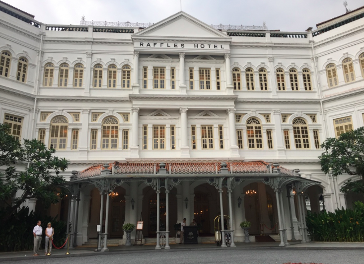 a large white building with many windows with Raffles Hotel in the background