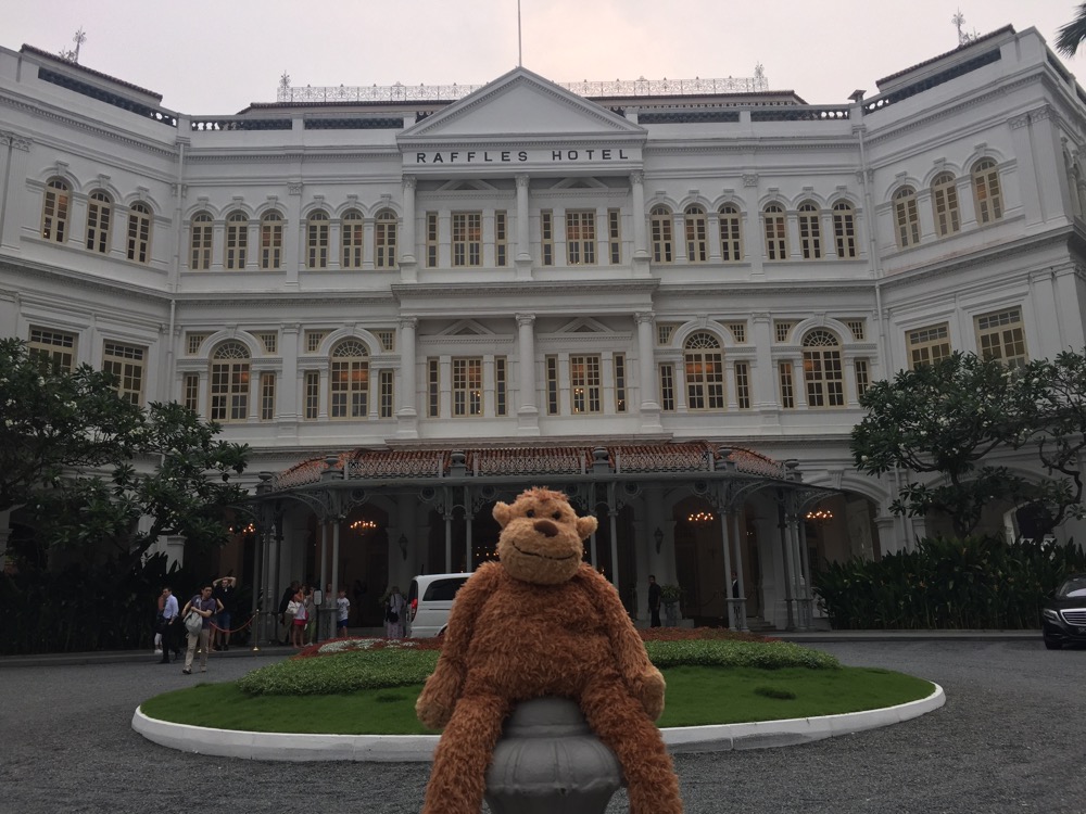 a stuffed animal sitting on a post in front of a large white building with Raffles Hotel in the background
