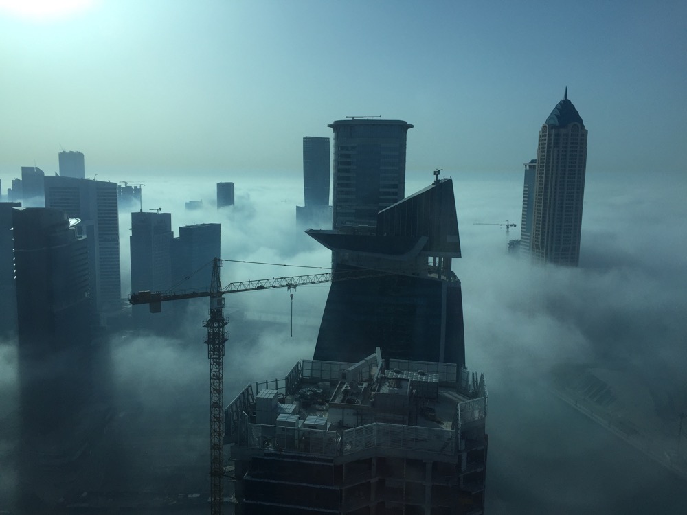 a tall buildings with a crane in the middle of clouds