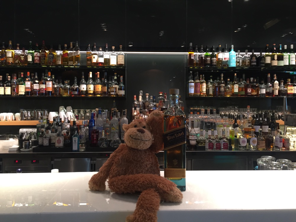 a stuffed animal sitting on a bar counter with bottles of liquor