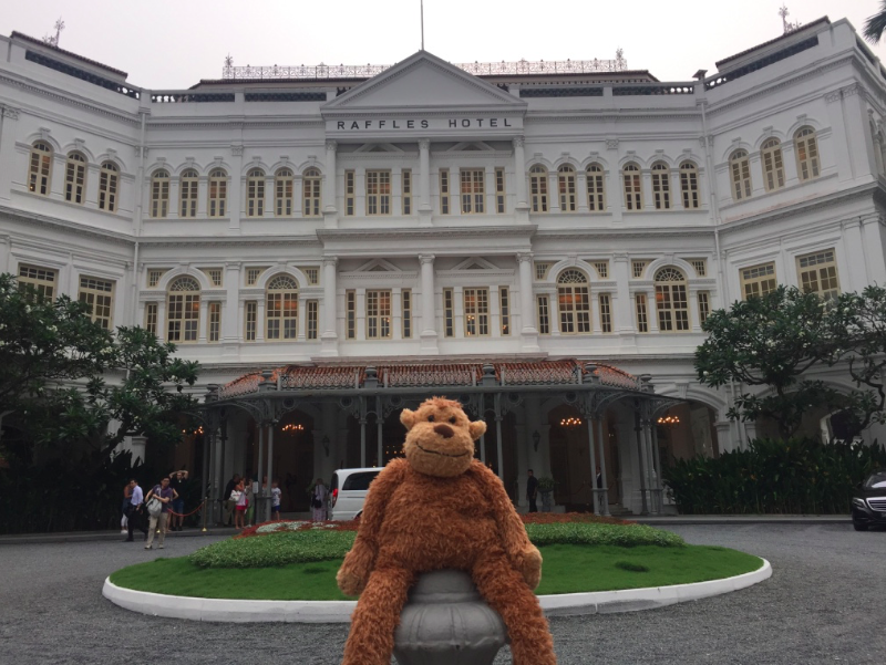 a stuffed animal sitting on a post in front of a large white building with Raffles Hotel in the background