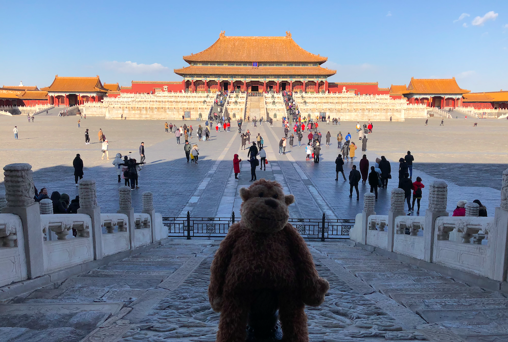a stuffed animal in front of a large building with Forbidden City in the background