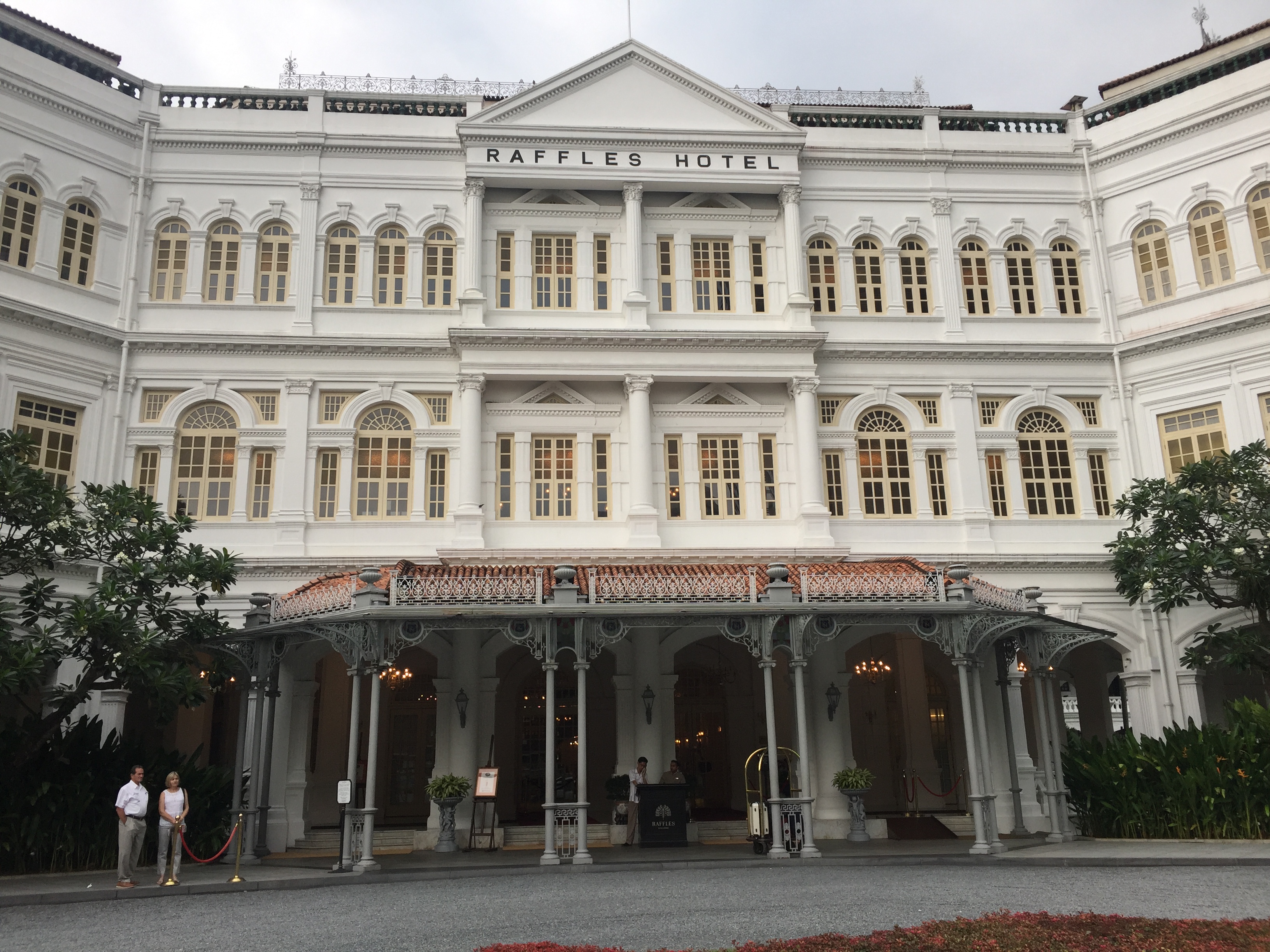 a large white building with a couple people standing in front of it with Raffles Hotel in the background