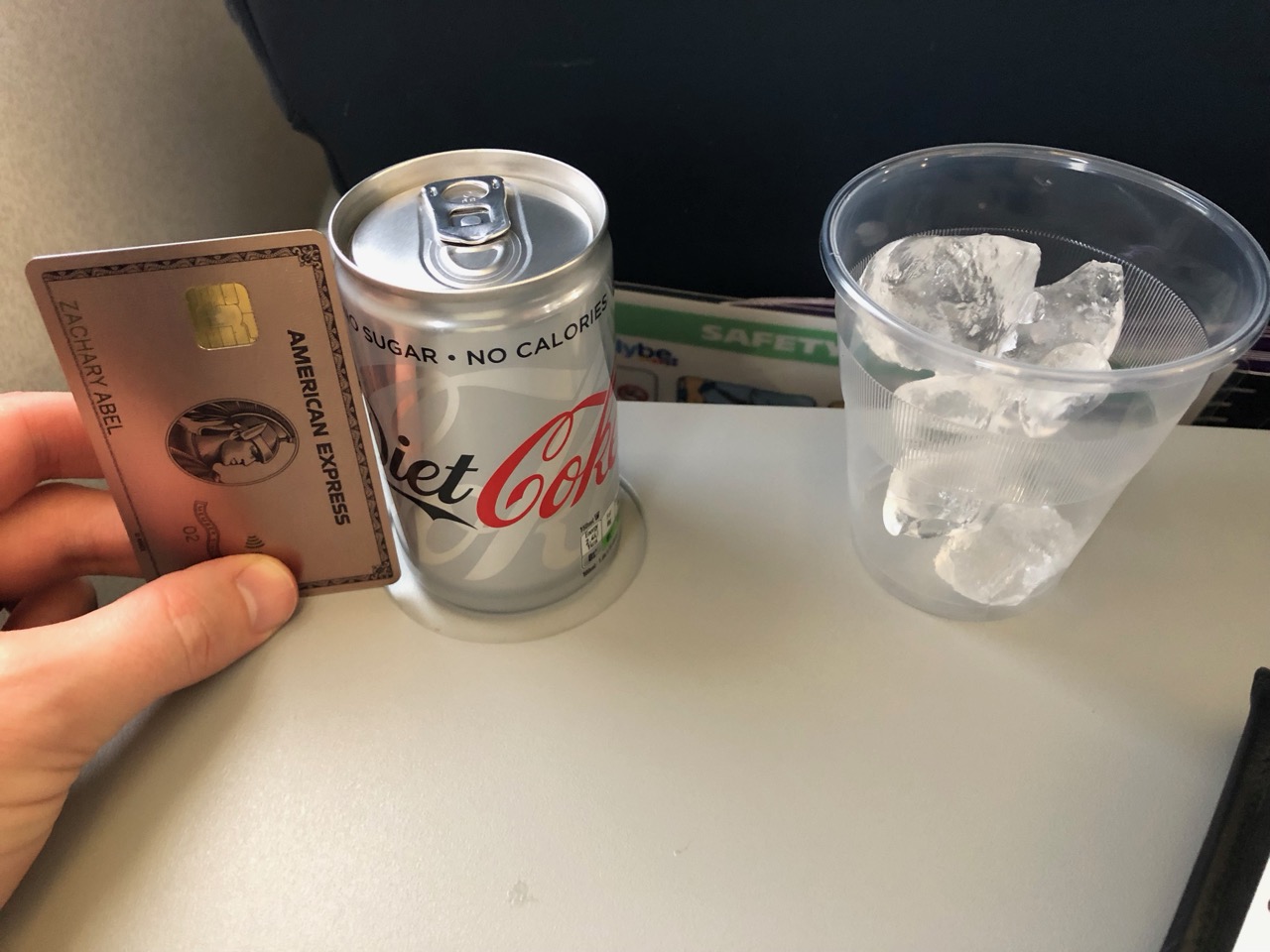 a hand holding a credit card and a soda can next to a plastic cup