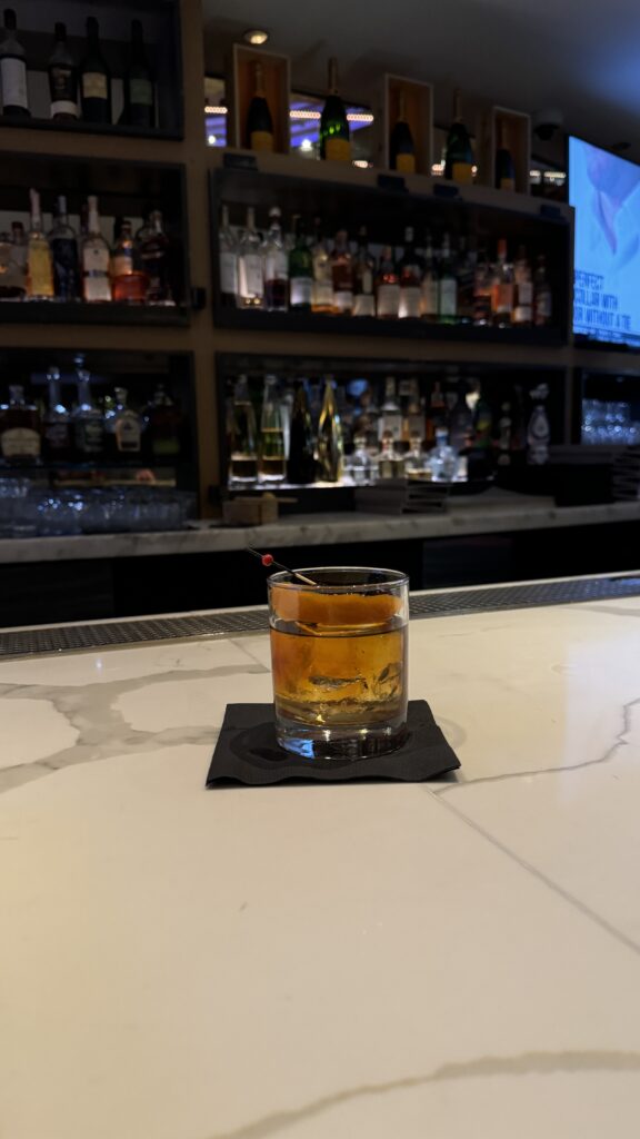 a glass of brown liquid on a black coaster on a white surface