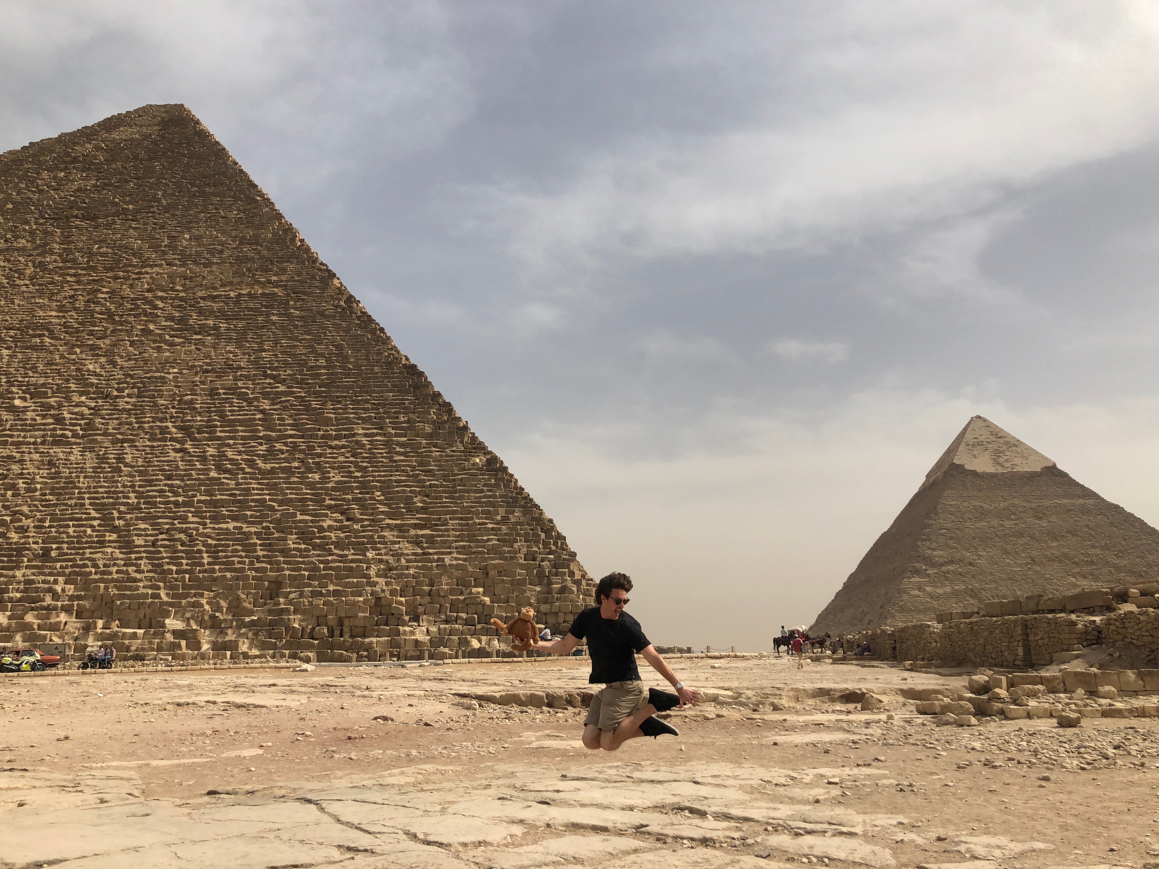 a man jumping in the sand with pyramids in the background