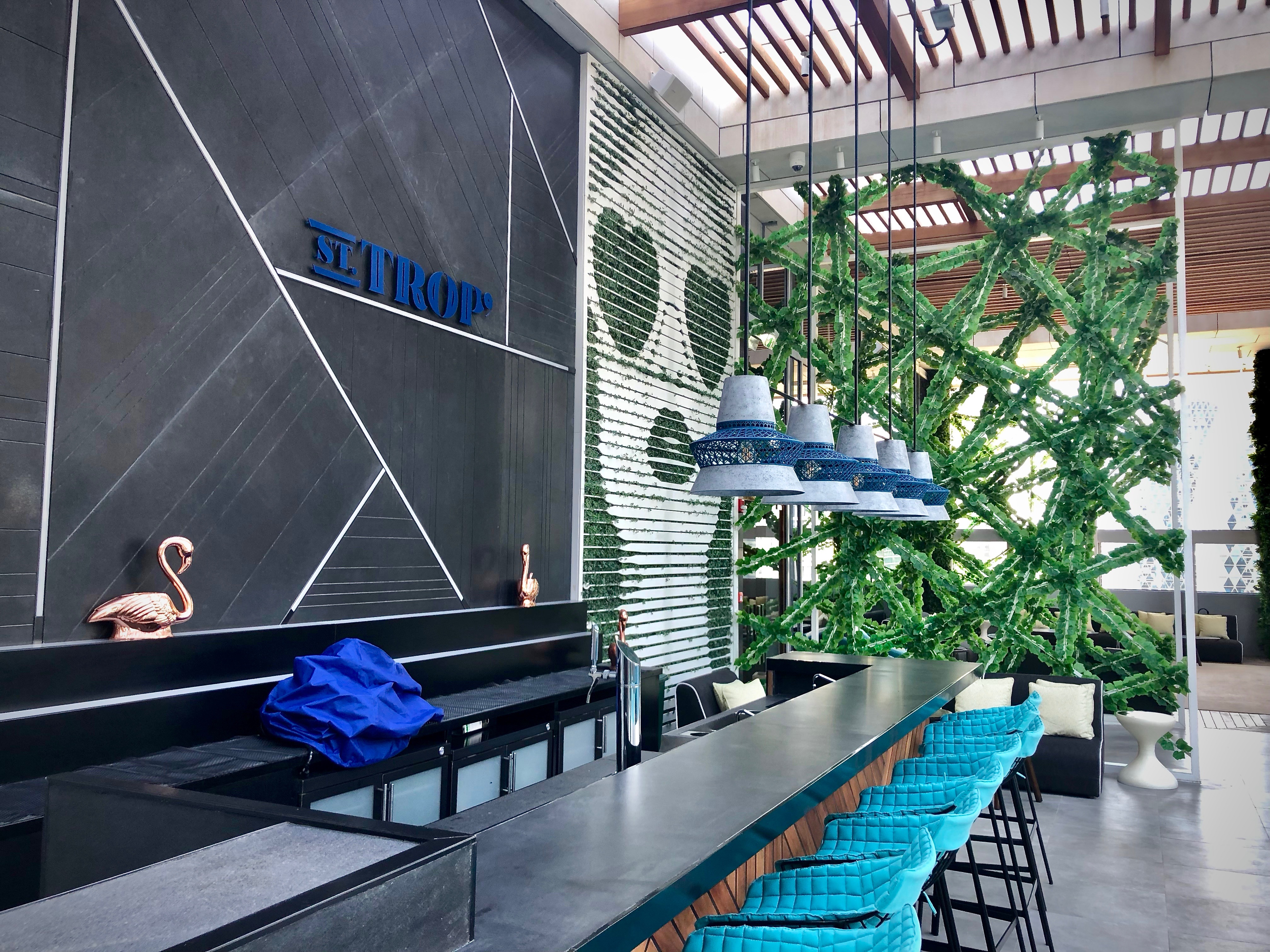 a bar with blue chairs and a wall with green plants