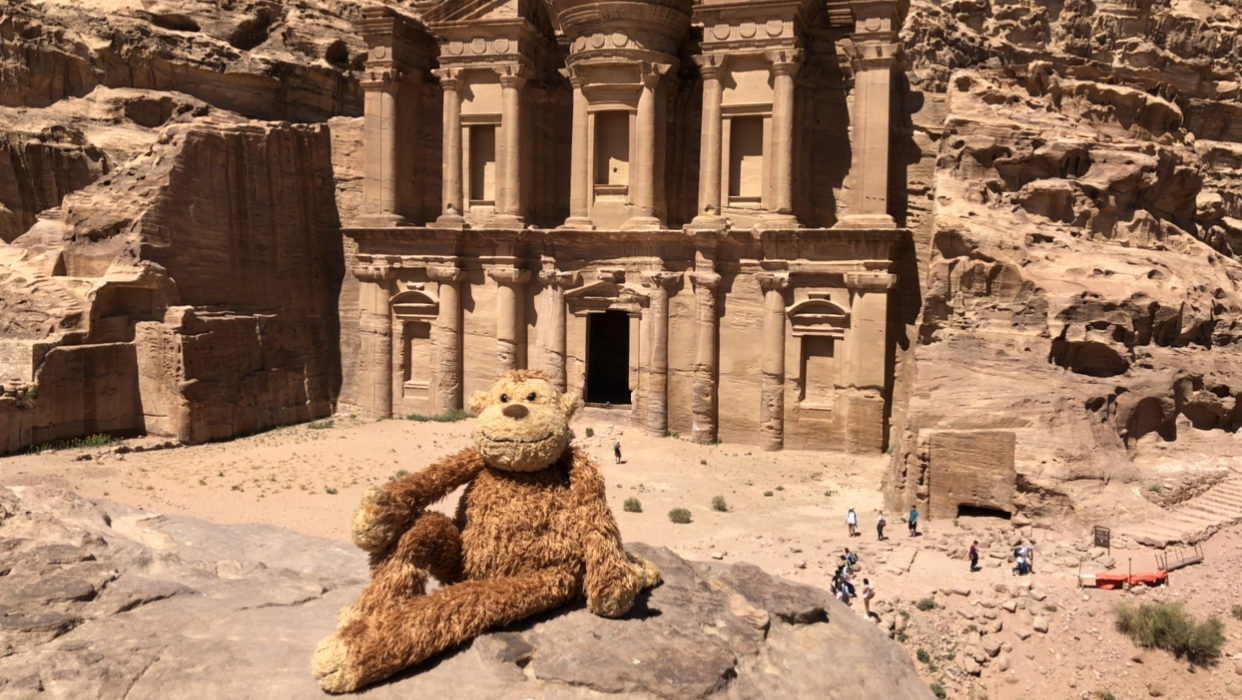 a stuffed animal sitting on a rock in front of a stone building with Petra in the background