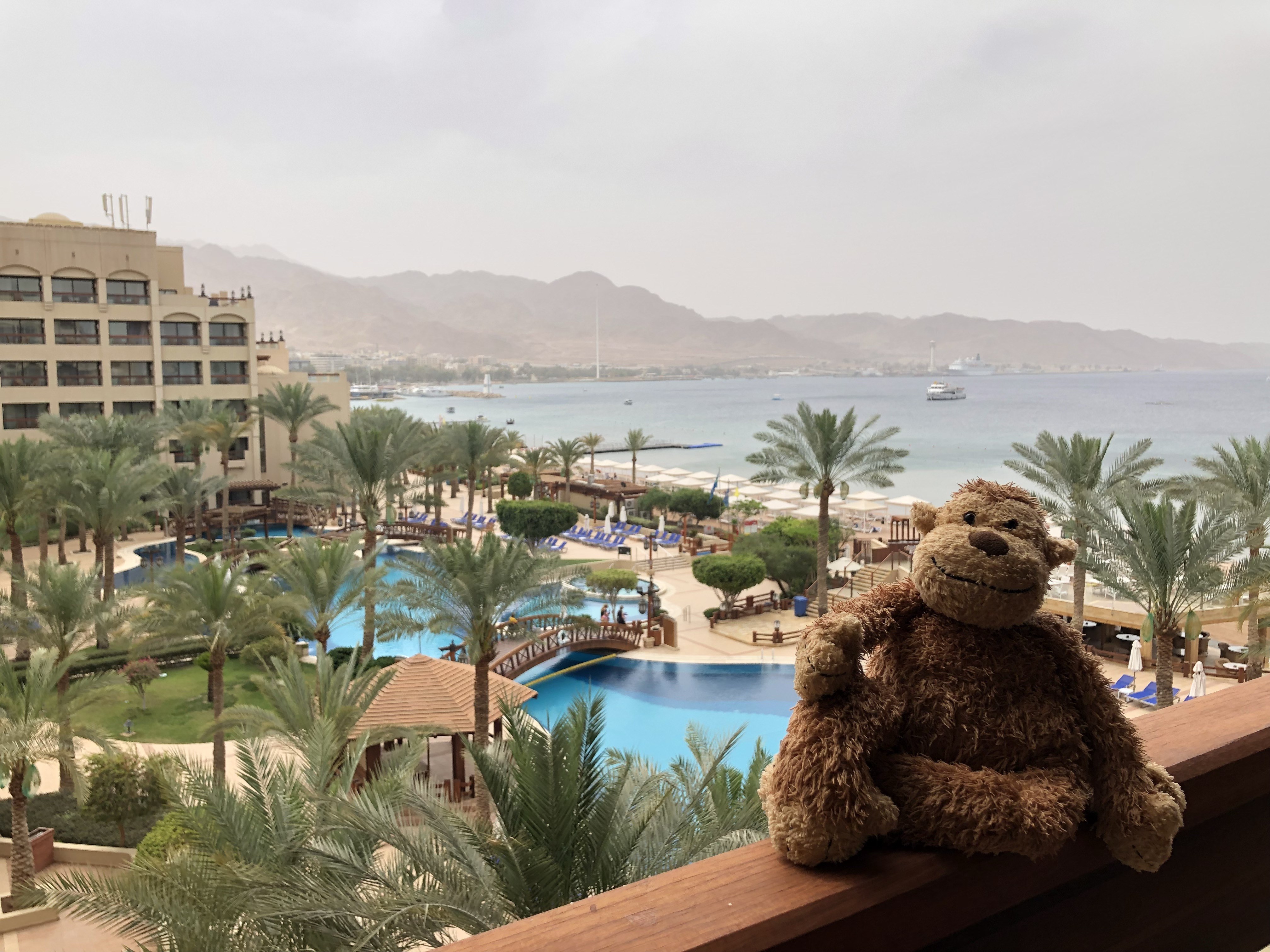 a teddy bear sitting on a railing overlooking a resort