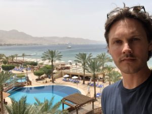 a man taking a selfie with a pool and mountains in the background