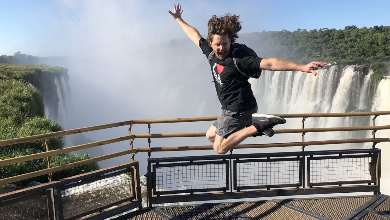 a man jumping in the air with a waterfall in the background