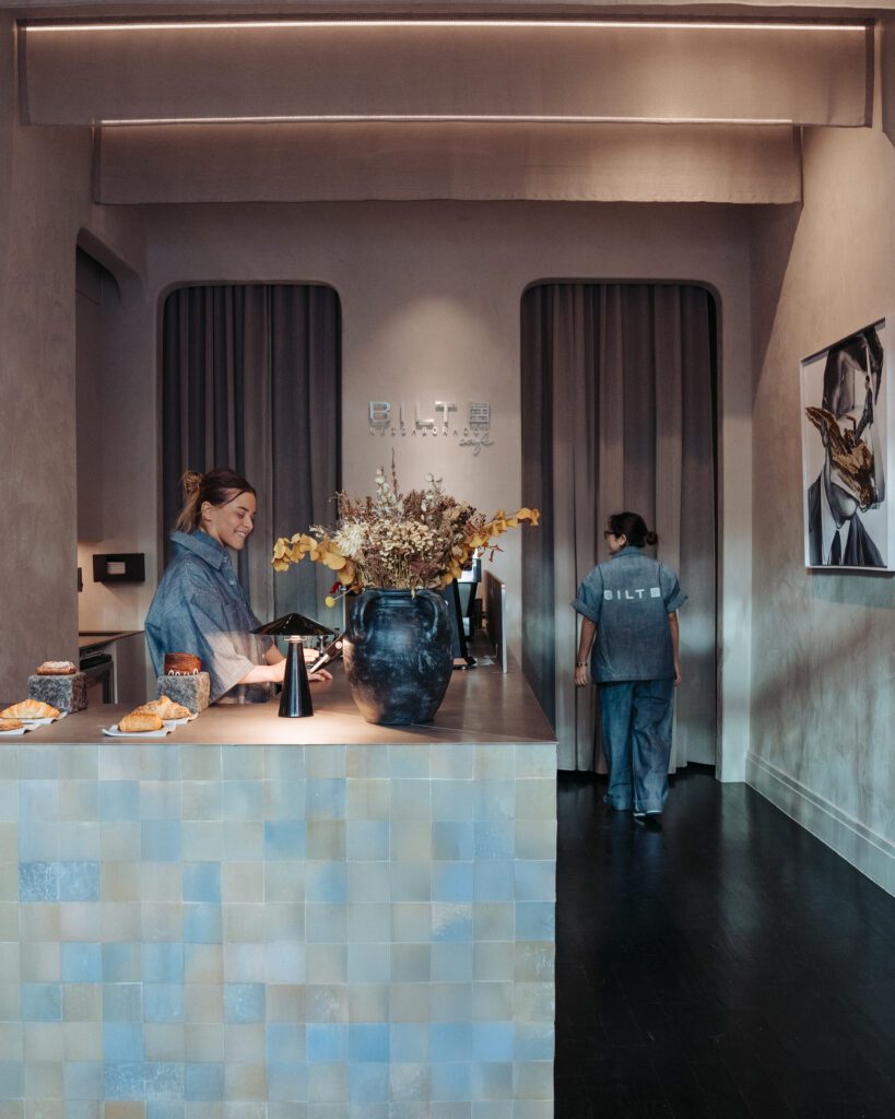 a woman standing at a counter in a room with a vase of flowers