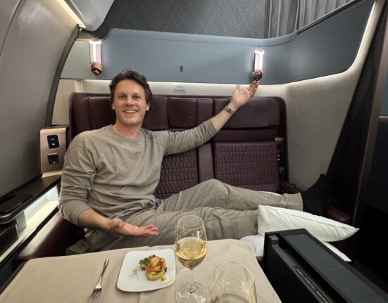 a man sitting in a chair with a plate of food and glasses on it